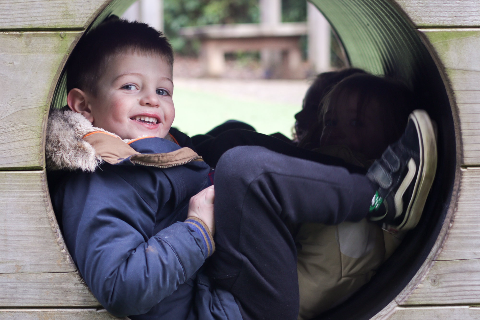 Boy sat in climbing tunnel smiling at camera