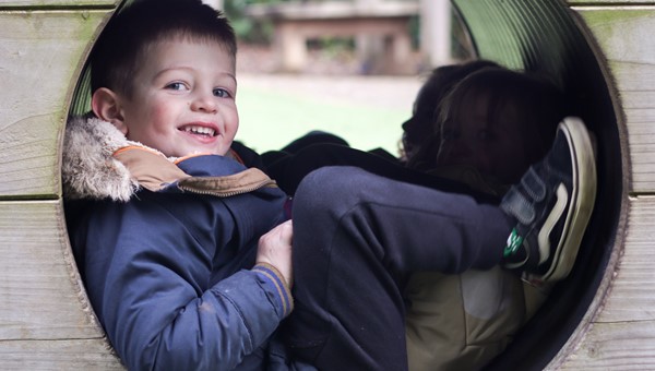 Boy sat in climbing tunnel smiling at camera