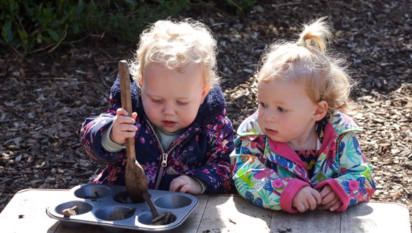 Two children playing outside in mud kitchen