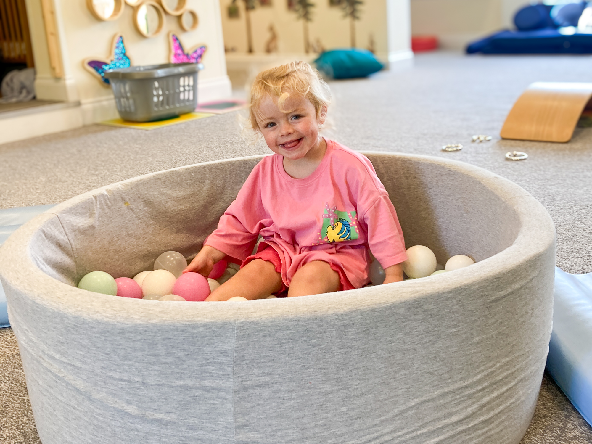 Baby sat in ballpit in nursery room smiling