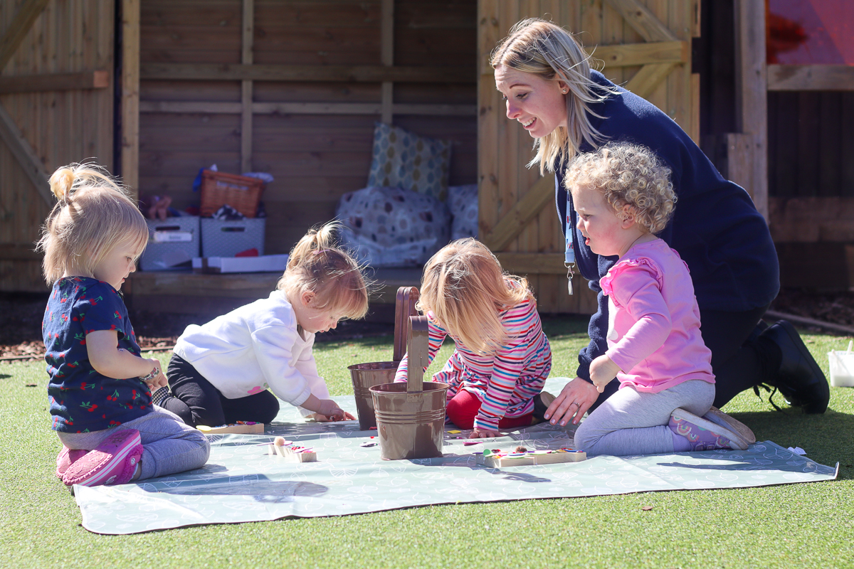 nursery practitioner playing with four children outside in garden arts and crafts