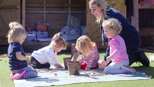 nursery practitioner playing with four children outside in garden arts and crafts